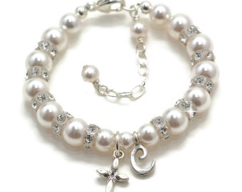 May include: A white pearl bracelet with a silver clasp and a silver charm with a cross and a letter C. The bracelet is decorated with small silver rhinestones.