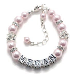 Peut inclure: Un bracelet personnalisé composé de perles nacrées rose clair, d'entretoises argentées avec des cristaux transparents et de perles carrées argentées formant le prénom MEGAN. Le bracelet comprend une chaînette d'extension en métal argenté.