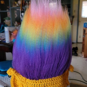 May include: A crocheted troll hat with a rainbow colored yarn wig. The hat is yellow and the wig is pink, orange, yellow, green, blue, and purple.