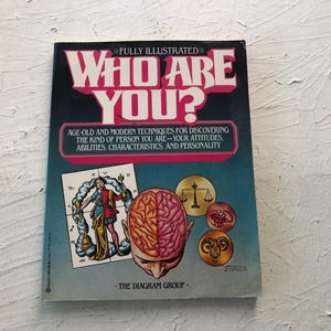 以下が含まれることがあります： Who Are You? Fully Illustratedというタイトルのペーパーバック本。青いグラデーションの表紙には、2色に分かれた脳、ローブを着た人物、天秤、サソリ、羊の頭が描かれた円形のアイコンが中央に配置されています。