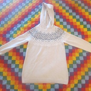 May include: A white hooded sweater with a black and white geometric pattern on the chest.