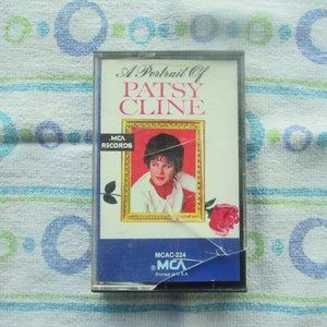 Op de afbeelding: Een cassettebandje met een portret van Patsy Cline op de voorkant. De cassette is zwart met een blauw-wit label. Het label heeft de tekst "A Portrait of Patsy Cline" en "MCA Records".