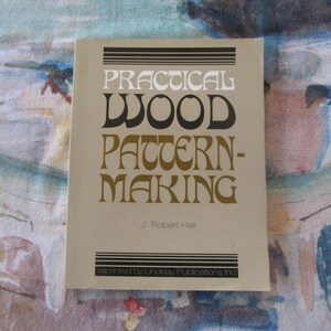 Può includere: Un libro beige intitolato "Practical Wood Pattern-Making" di J. Robert Hall. La copertina del libro presenta testo nero e dorato.