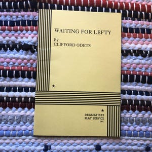 May include: A vintage playbill titled "Waiting for Lefty" by Clifford Odets. The cover is a light yellow with black text and vertical stripes on the left side. The playbill is on a multi-coloured woven rug.