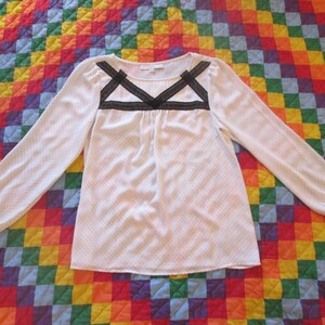 May include: White long-sleeved blouse with a black lace trim around the neckline. The blouse has a dotted pattern.