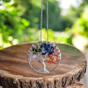 Puede incluir: Un collar con colgante plateado con un dise&ntilde;o de &aacute;rbol alambrado. El &aacute;rbol est&aacute; adornado con piedras preciosas de colores, incluyendo rosa, verde, azul y naranja. El collar cuelga de una delicada cadena plateada, creando un accesorio inspirado en la naturaleza.