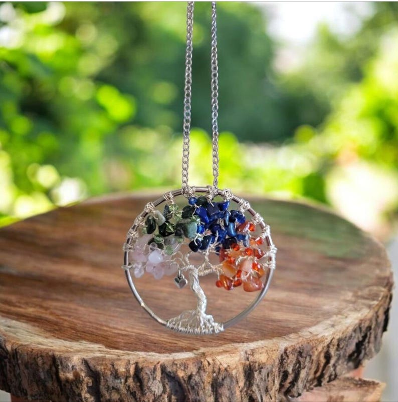 Puede incluir: Un collar con colgante plateado con un dise&ntilde;o de &aacute;rbol alambrado. El &aacute;rbol est&aacute; adornado con piedras preciosas de colores, incluyendo rosa, verde, azul y naranja. El collar cuelga de una delicada cadena plateada, creando un accesorio inspirado en la naturaleza.