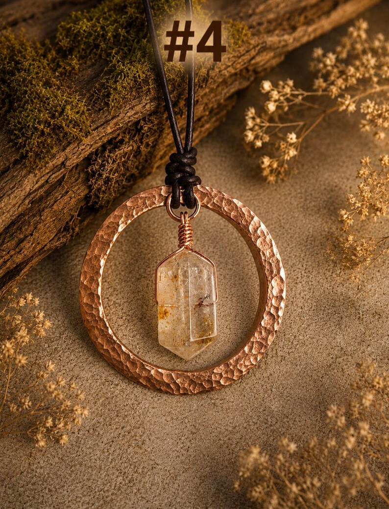May include: A necklace featuring a hammered copper ring pendant suspended from a black leather cord. A clear, faceted crystal point is wrapped in copper wire and hangs from the center of the ring. The image includes the text #4.