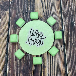 May include: A circle with the text "Lime Frost" in white lettering on a light green background.  Eight small, square, light green watercolor paint pans are arranged around the circle.