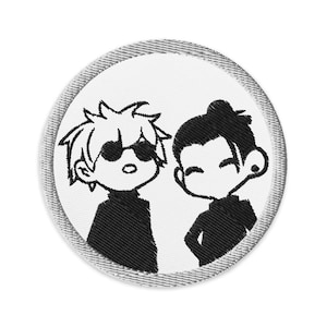 Op de afbeelding: Ronde geborduurde patch met een witte kern en een grijze rand. De patch toont twee cartoonfiguren in zwart en wit. Eén figuur draagt een zonnebril, de ander heeft haar in een knot.