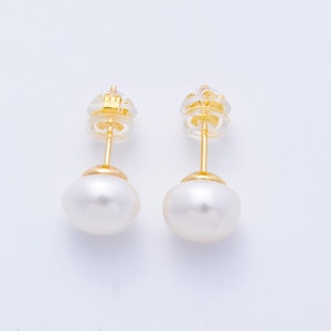 May include: A pair of stud earrings featuring smooth, white, round pearls mounted on gold-toned metal posts. Each earring includes a clear, circular plastic backing attached to the post, providing a secure fit for the pearl and metal hardware.
