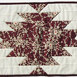 Puede incluir: Dos manteles individuales acolchados con un patrón geométrico burdeos y blanco. El patrón presenta un diseño de estrella con fondo blanco y detalles burdeos.