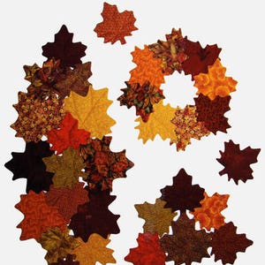 May include: A collection of fabric fall leaves in various shades of brown, orange, and yellow. The leaves are arranged in a circle and a cluster, creating a festive autumnal display.