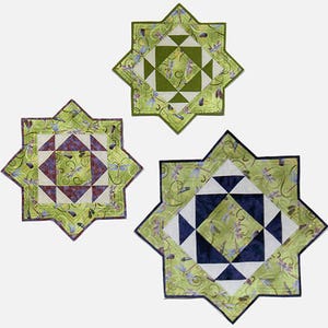 Op de afbeelding: Drie stervormige, gestikte placemats in groen, wit en blauw met libellenmotieven.