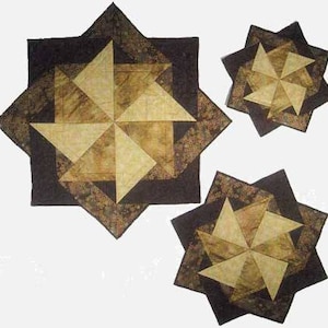 Può includere: Tre elementi trapuntati a forma di stella nei toni del marrone e del beige. Il più grande ha un centro quadrato con un disegno a stella, circondato da un bordo marrone scuro. Sono visibili anche due stelle più piccole, che mostrano lo stesso design e la stessa tavolozza di colori.