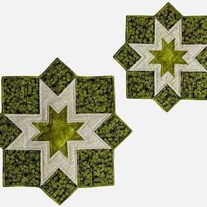 May include: Two green and white star-shaped quilted placemats. The placemats are made of fabric with a leafy pattern. The larger placemat is about 30 cm in diameter, and the smaller placemat is about 20 cm in diameter.
