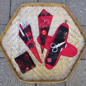 May include: Three fabric sewing needle cases with black and red geometric patterns. One case holds scissors, another holds needles and thread, and the third holds a variety of sewing tools.