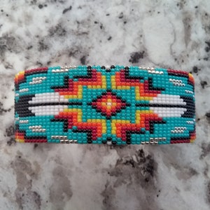 May include: A turquoise, red, yellow, white, and black beaded hair clip with a geometric pattern.