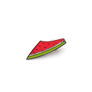 Puede incluir: Un broche de esmalte metálico con forma de rodaja de sandía. El broche presenta una sección triangular de color rojo brillante con pequeños puntos negros que representan semillas, bordeada por una línea blanca fina y una corteza verde.