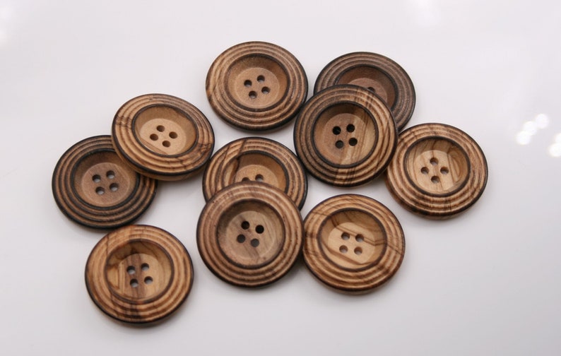 May include: Ten wooden buttons with a brown and light brown wood grain pattern. Each button has four holes and a raised center.