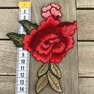 May include: Red and pink embroidered flower applique with green and gold leaves. The applique is approximately 6 inches tall.