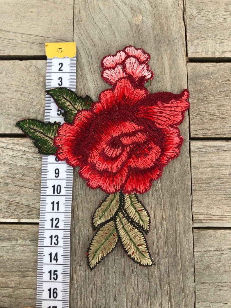 May include: Red and pink embroidered flower applique with green and gold leaves. The applique is approximately 6 inches tall.