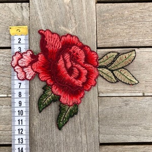 May include: Red embroidered rose applique with green leaves. The applique is approximately 6 inches wide and 5 inches tall.