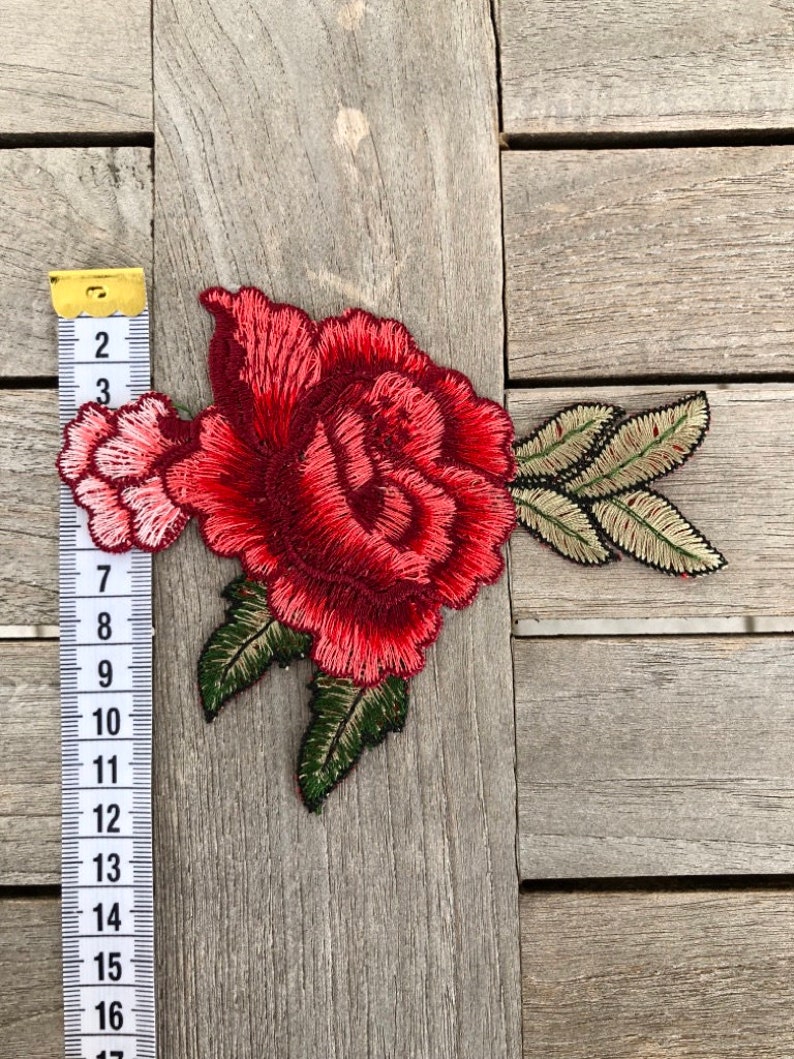 May include: Red embroidered rose applique with green leaves. The applique is approximately 6 inches wide and 5 inches tall.
