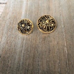 May include: Two gold-toned buttons with intricate floral designs. The larger button is slightly larger than the smaller button.
