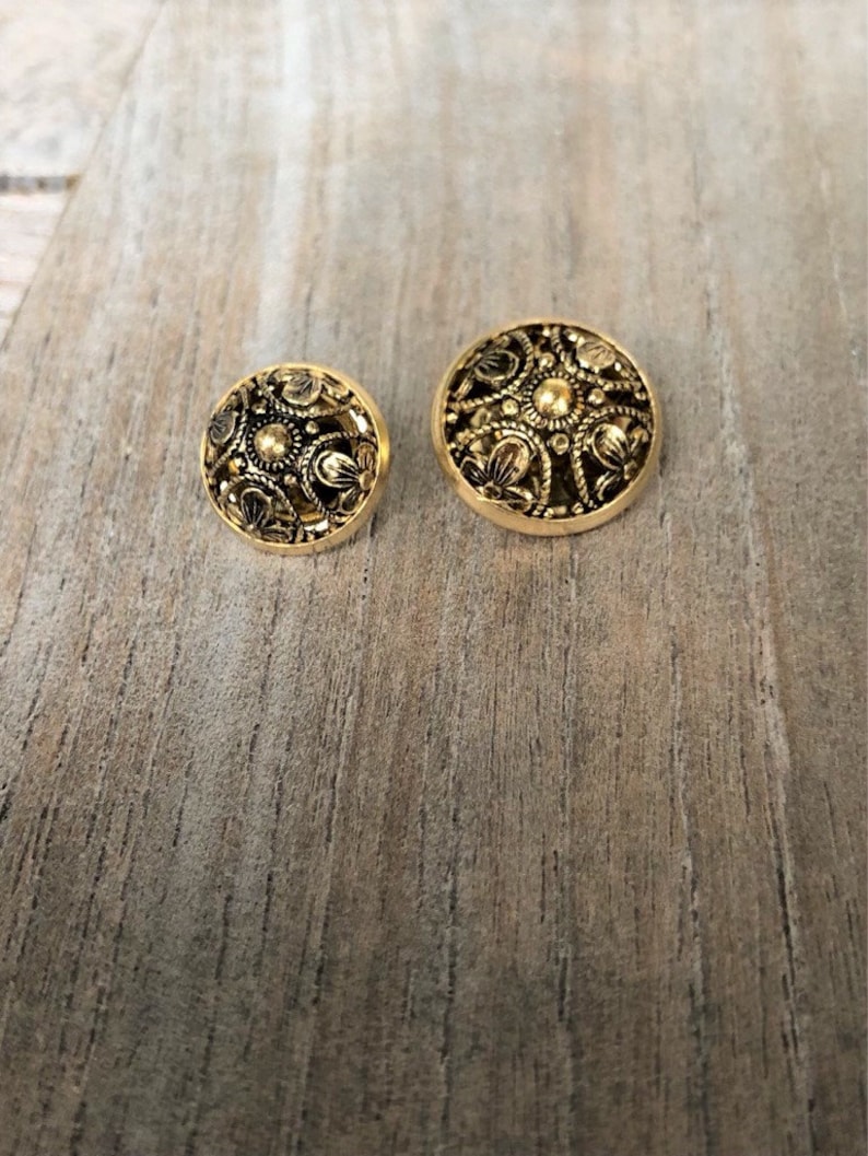 May include: Two gold-toned buttons with intricate floral designs. The larger button is slightly larger than the smaller button.