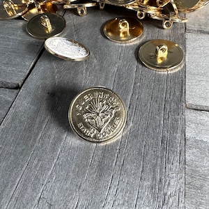 Könnte beinhalten: Ein goldfarbener Metallknopf mit einem erhabenen Design eines Kiefernbaums und den Worten "SELWYN STATE" und "SANTA CRUZ" um den Baum herum.