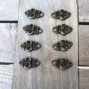 Può includere: Otto ornamenti decorativi in metallo color oro antico con un design floreale. Ogni ornamento ha un anello nella parte superiore per essere attaccato a un progetto.