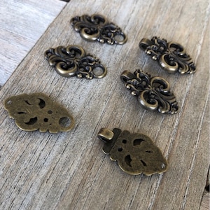 May include: A set of six antique gold-toned metal decorative embellishments with intricate floral designs. The embellishments have a vintage look and are perfect for adding a touch of elegance to crafts, jewelry, or clothing.