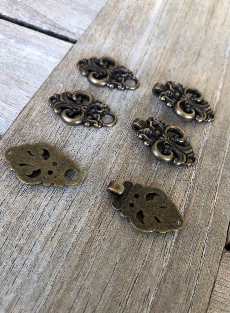 May include: A set of six antique gold-toned metal decorative embellishments with intricate floral designs. The embellishments have a vintage look and are perfect for adding a touch of elegance to crafts, jewelry, or clothing.