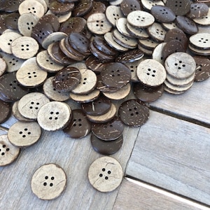 Peut inclure: Un tas de boutons en coquille de noix de coco brune et naturelle avec quatre trous chacun. Les boutons sont éparpillés sur une surface en bois.