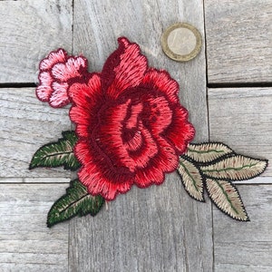 May include: A red embroidered rose with green leaves. The rose is about the size of a US quarter.