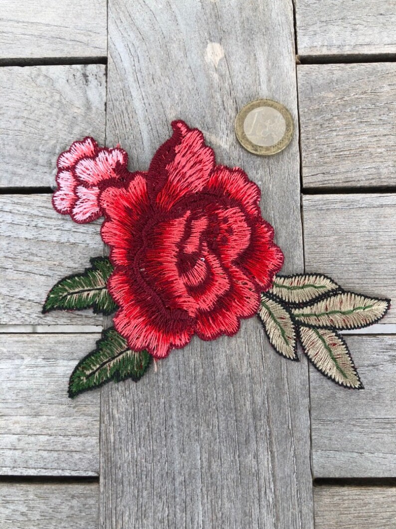 May include: A red embroidered rose with green leaves. The rose is about the size of a US quarter.