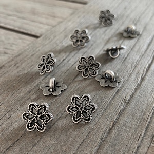 Könnte beinhalten: Eine Sammlung silberfarbener Metallknöpfe mit floralem Design. Die Knöpfe haben eine Öse auf der Rückseite zum Nähen.