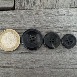 May include: Three black plastic buttons with four holes each. The buttons are arranged in a row from largest to smallest.