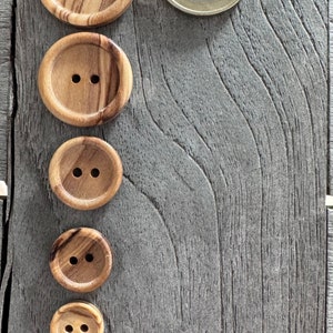 May include: Five wooden buttons of varying sizes with two holes each. The buttons are arranged vertically from largest to smallest on a gray wooden surface.