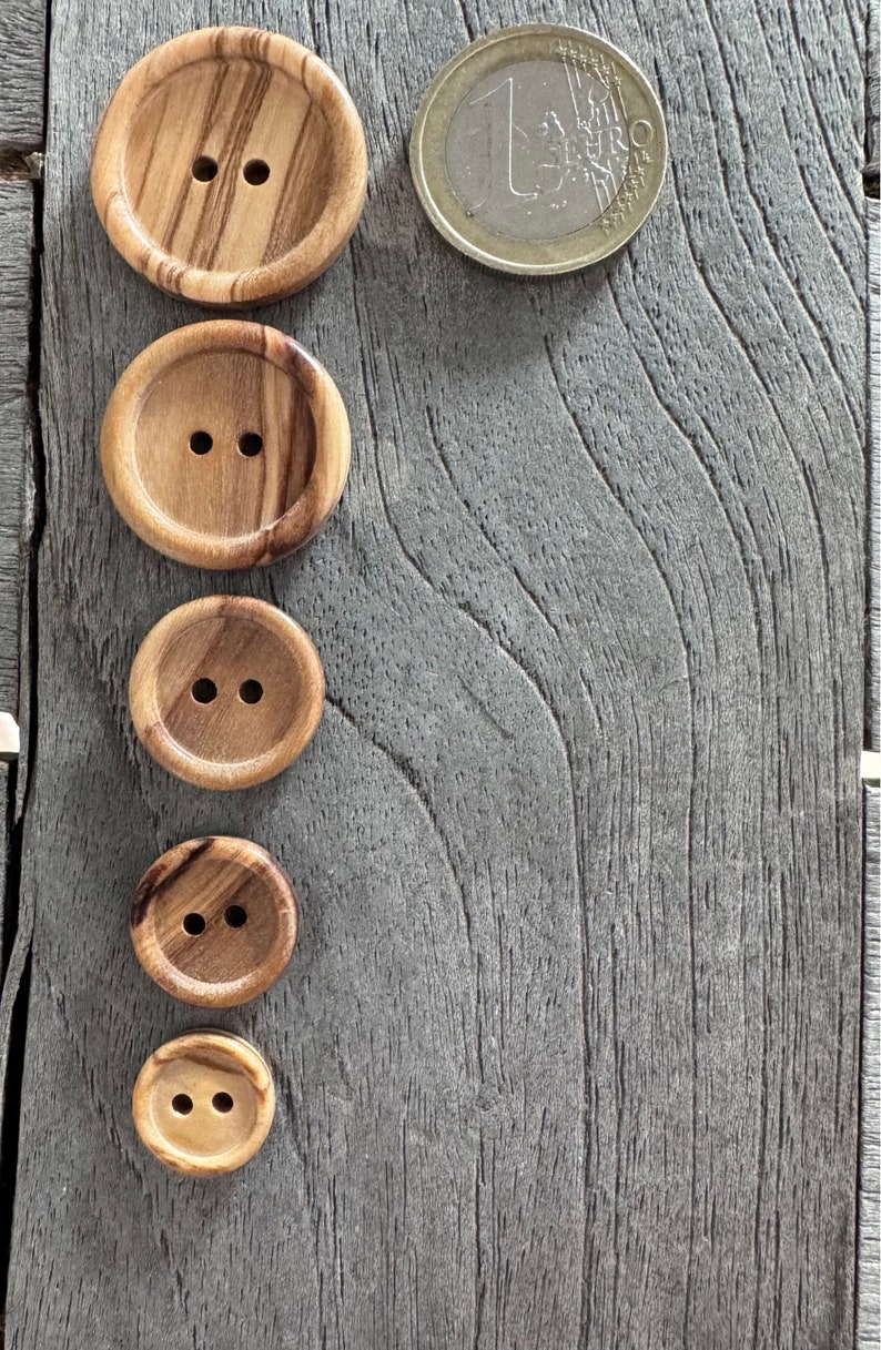 May include: Five wooden buttons of varying sizes with two holes each. The buttons are arranged vertically from largest to smallest on a gray wooden surface.