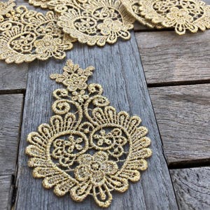 May include: Gold lace trim with a delicate floral pattern. The lace is arranged in a decorative pattern on a wooden surface.