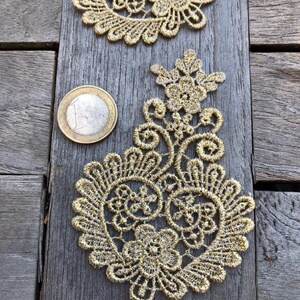 May include: Gold lace trim with a paisley design. The lace is delicate and intricate, with a floral pattern. The trim is approximately 5 cm in diameter.