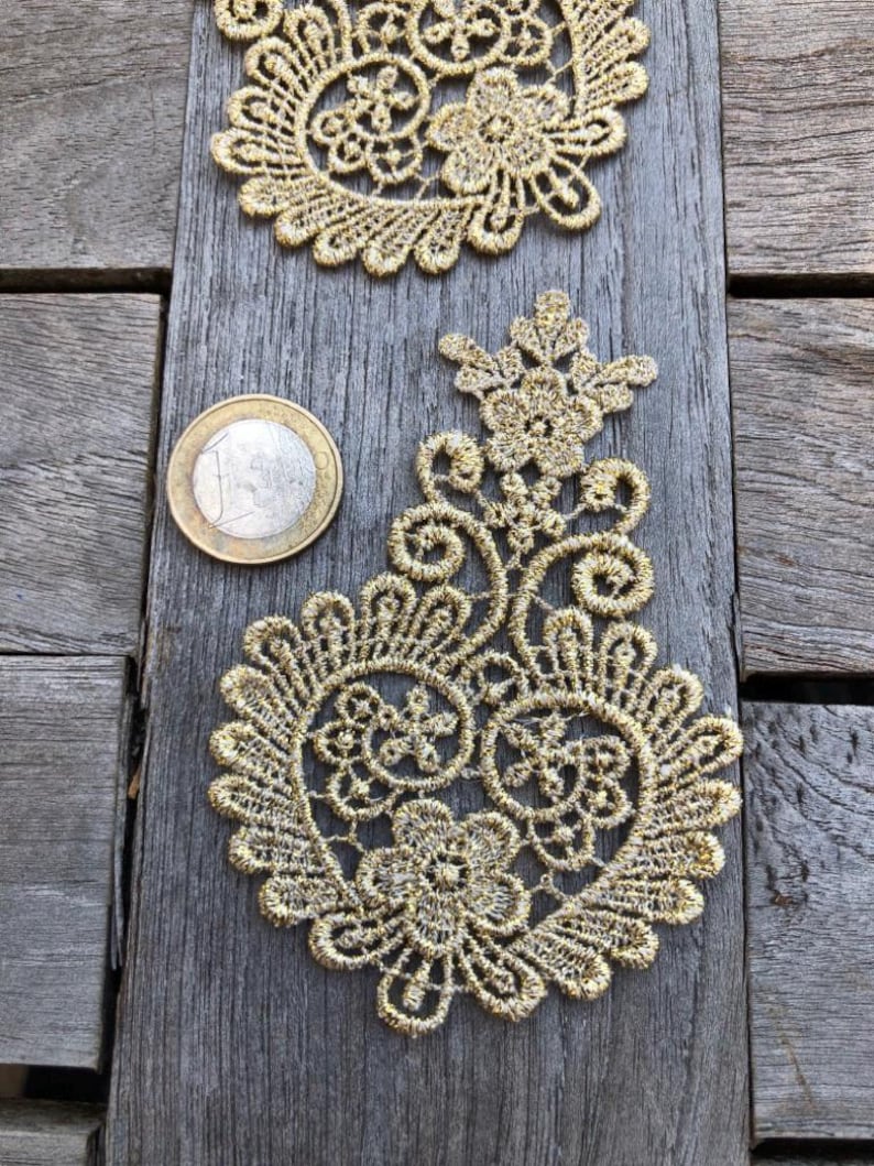 May include: Gold lace trim with a paisley design. The lace is delicate and intricate, with a floral pattern. The trim is approximately 5 cm in diameter.