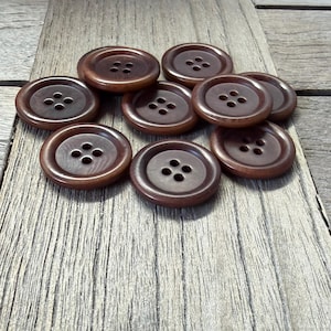 Op de afbeelding: Een verzameling bruine, ronde knopen met elk vier gaatjes. De knopen liggen op een houten oppervlak, waarbij hun glanzende afwerking en klassieke ontwerp worden getoond. Ideaal voor naai- en knutselprojecten.