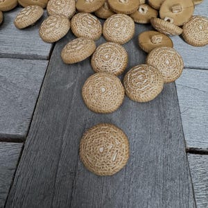 May include: A pile of beige crocheted buttons with a white center. The buttons are arranged in a random pattern on a wooden surface.