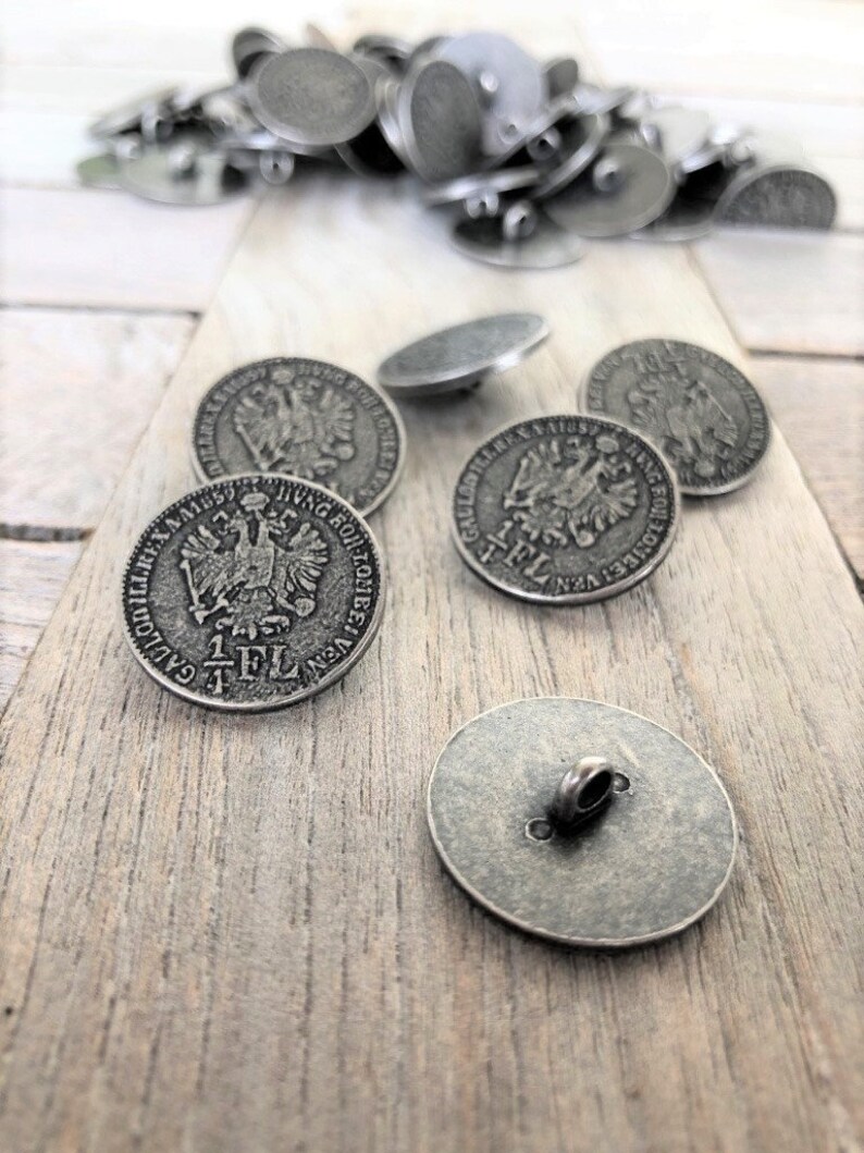 May include: A group of silver-toned metal buttons with a raised design of an eagle and the text "1 FL" on the front. The buttons have a loop on the back for sewing.