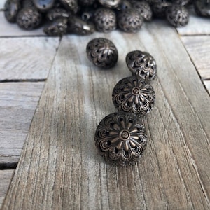 Könnte beinhalten: Vier verzierte, dunkelbraune Knöpfe mit einem dekorativen Blumenmuster. Die Knöpfe sind in einer Reihe auf einer Holzoberfläche angeordnet.