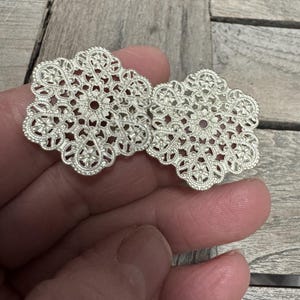 Könnte beinhalten: Zwei silberne Filigranverzierungen mit quadratischer Form und filigranen Blumendesigns.