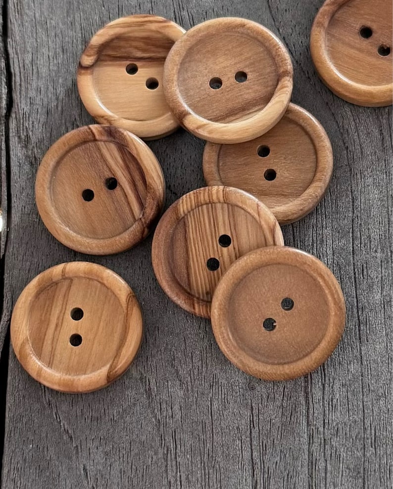 May include: A collection of eight wooden buttons with two holes each. The buttons are round and have a natural wood grain pattern. They are a light brown color.